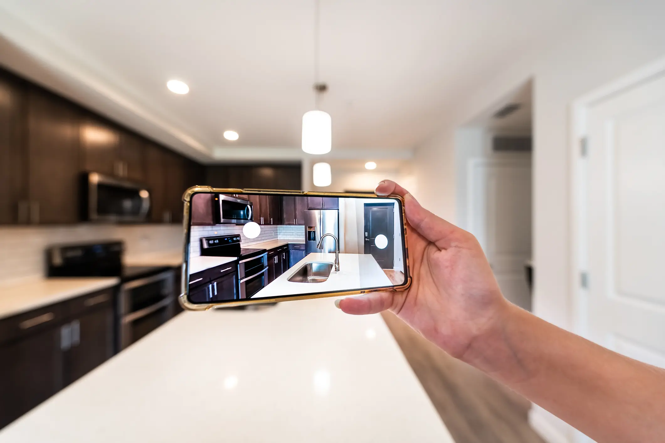 Hand holding phone photographing modern kitchen.