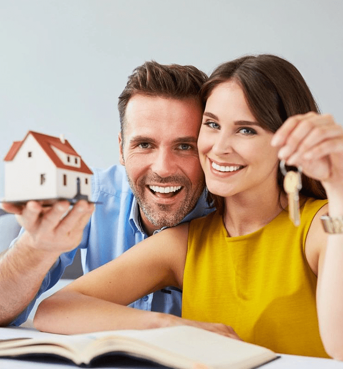 A smiling couple holding house keys and a small house model, indicating the purchase of a new home.