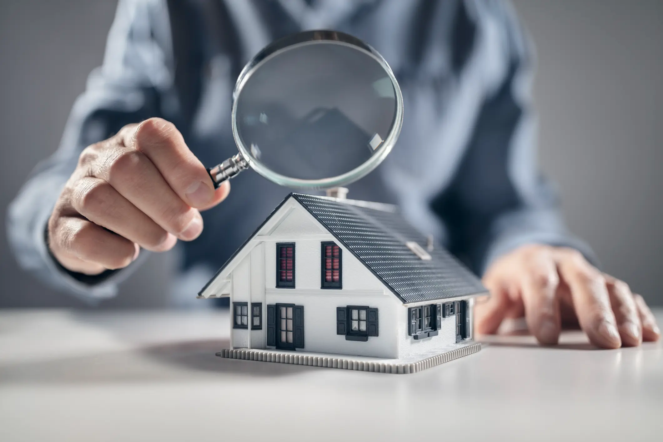 Person examining house model with magnifying glass.